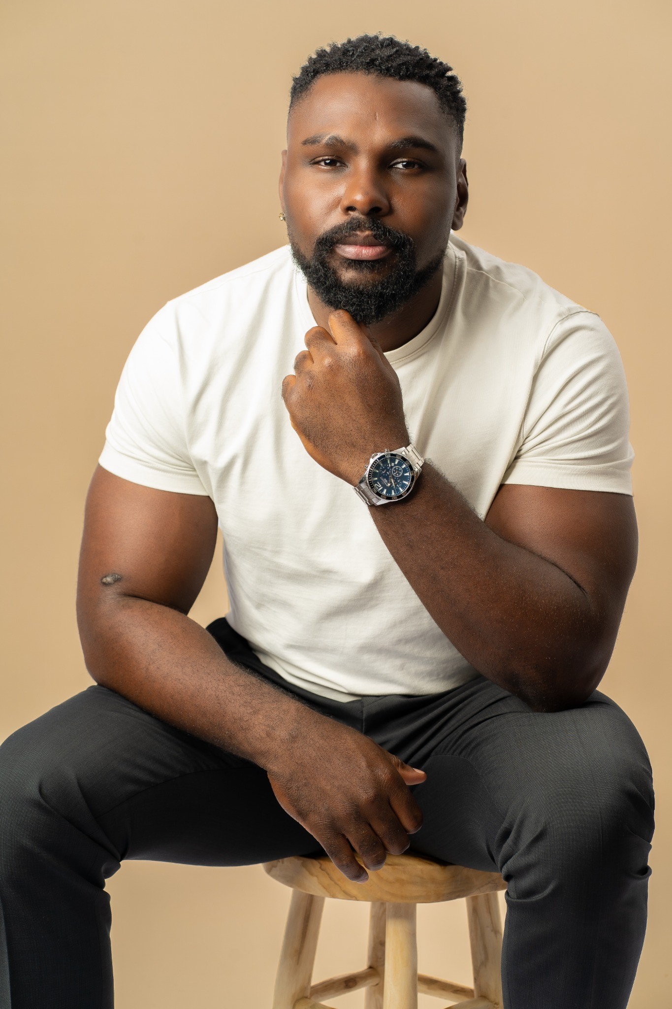 Chris Kibuka assis en studio, la main au menton