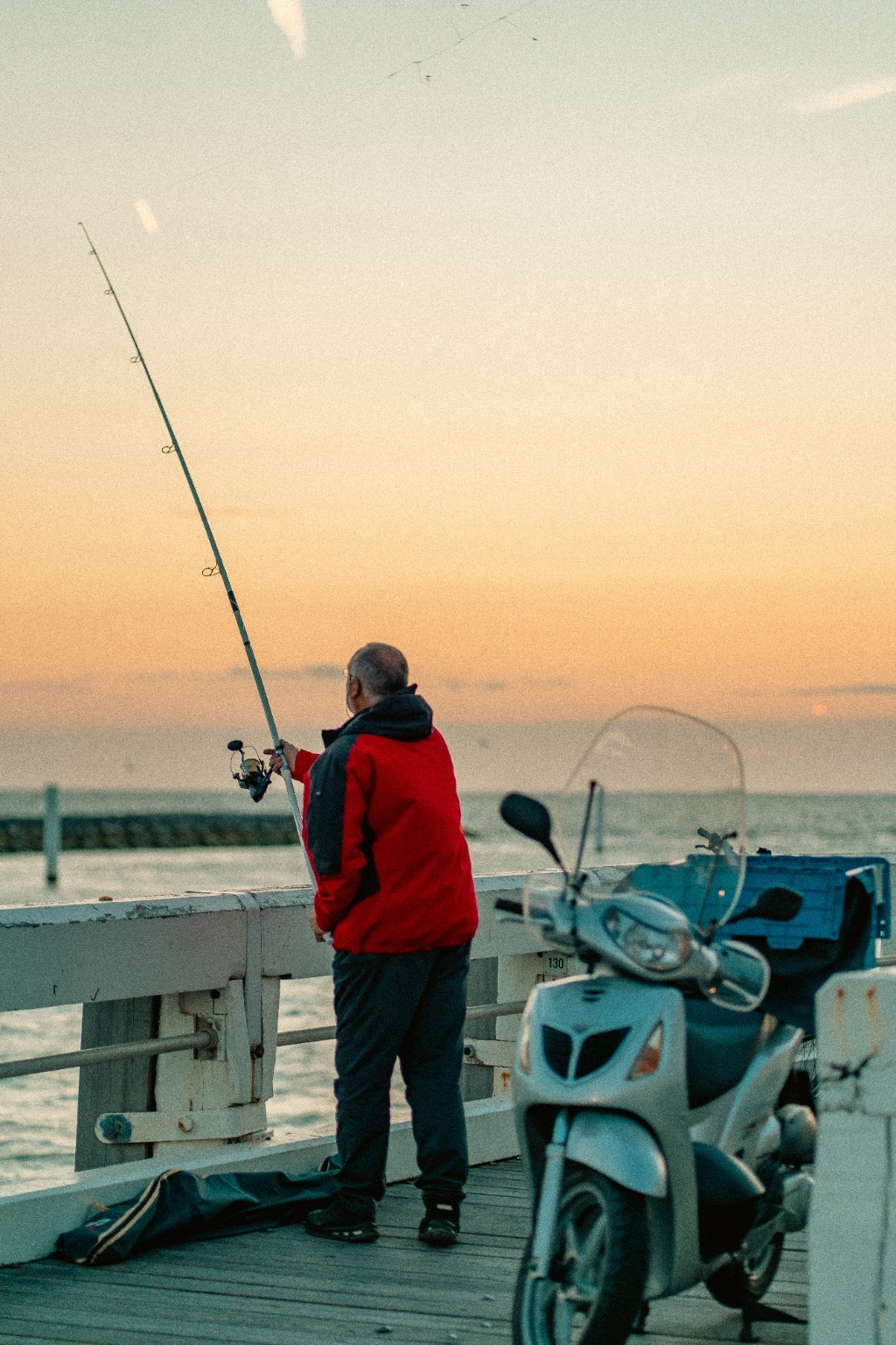 Un pêcheur et un scooter face à la mer au coucher du soleil